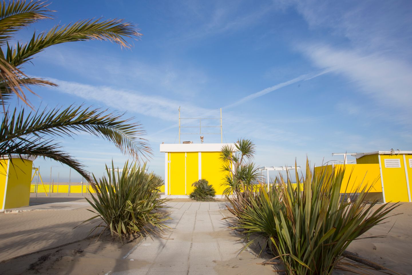 Cabañas de playa amarillas brillantes y plantas tropicales bajo un cielo azul claro en Rimini, Italia.