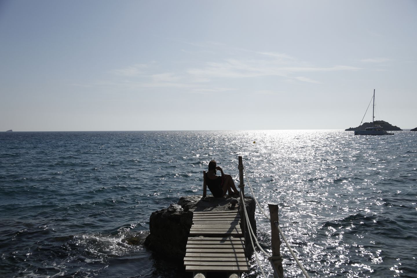 Una silueta tranquila en un muelle de madera en Ibiza contra un resplandeciente atardecer sobre el océano.