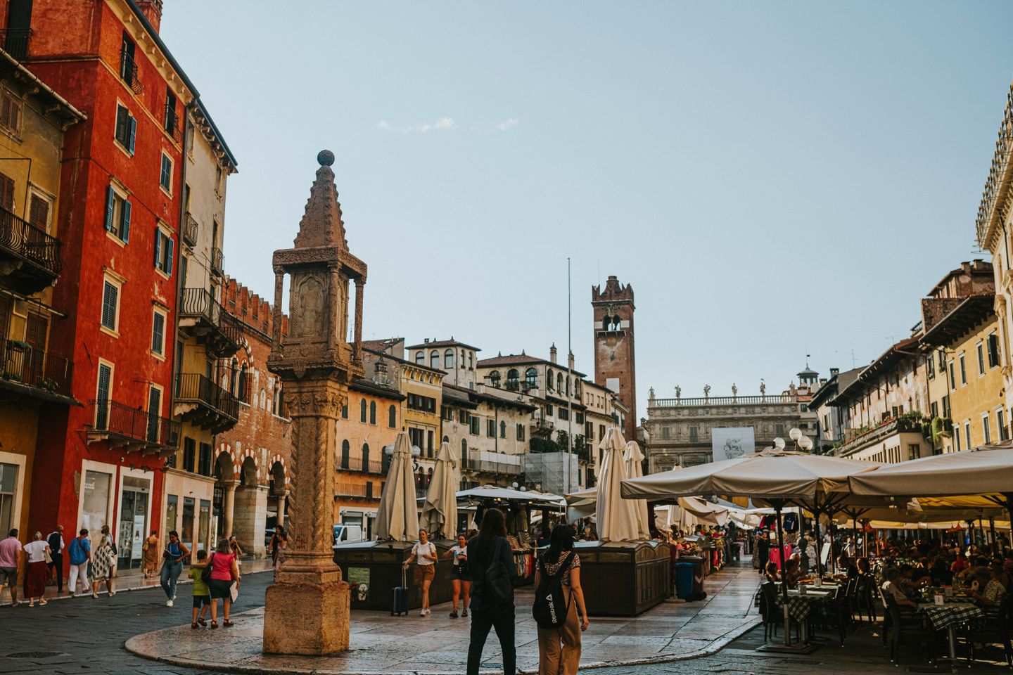 La bulliciosa Piazza delle Erbe en el centro histórico de Verona, con turistas explorando entre la vibrante arquitectura.