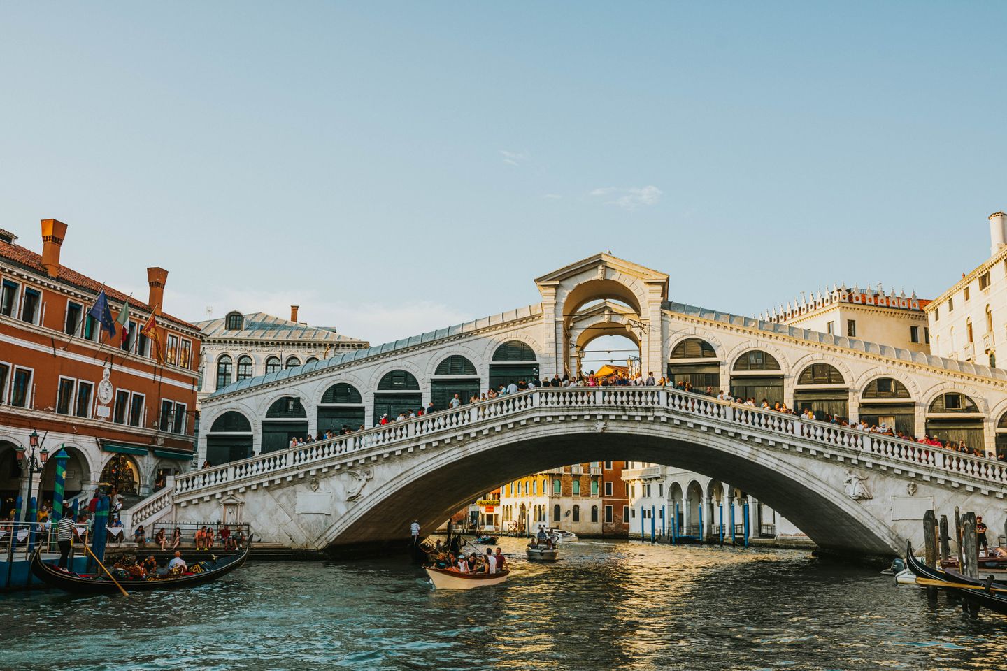 El icónico Puente de Rialto que cruza el Gran Canal en Venecia, bañado por la luz del día, con góndolas pasando por debajo.