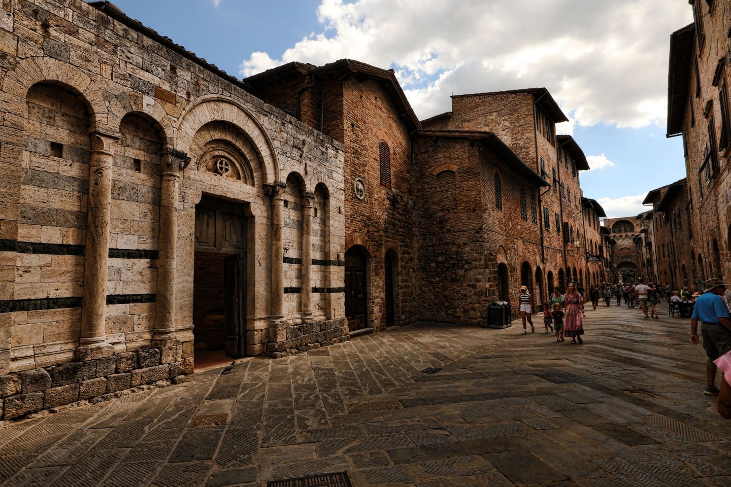 Encantadora escena callejera medieval en San Gimignano, mostrando arquitectura histórica bajo un cielo azul.