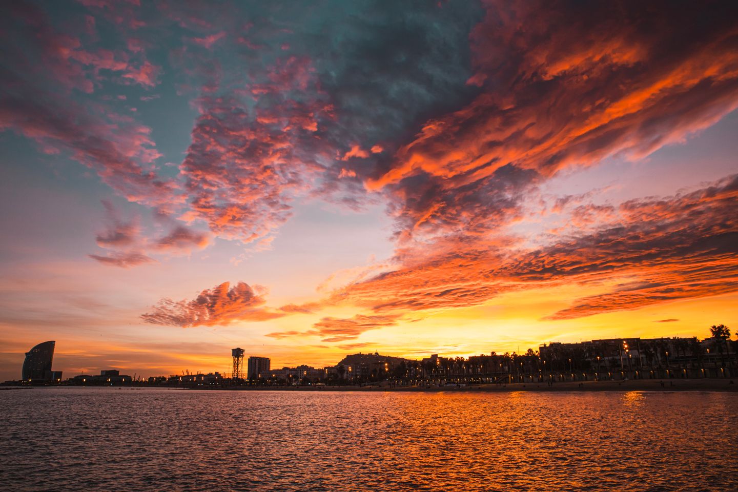 Impresionante atardecer sobre la playa de Barcelona con nubes dramáticas y el horizonte de la ciudad.