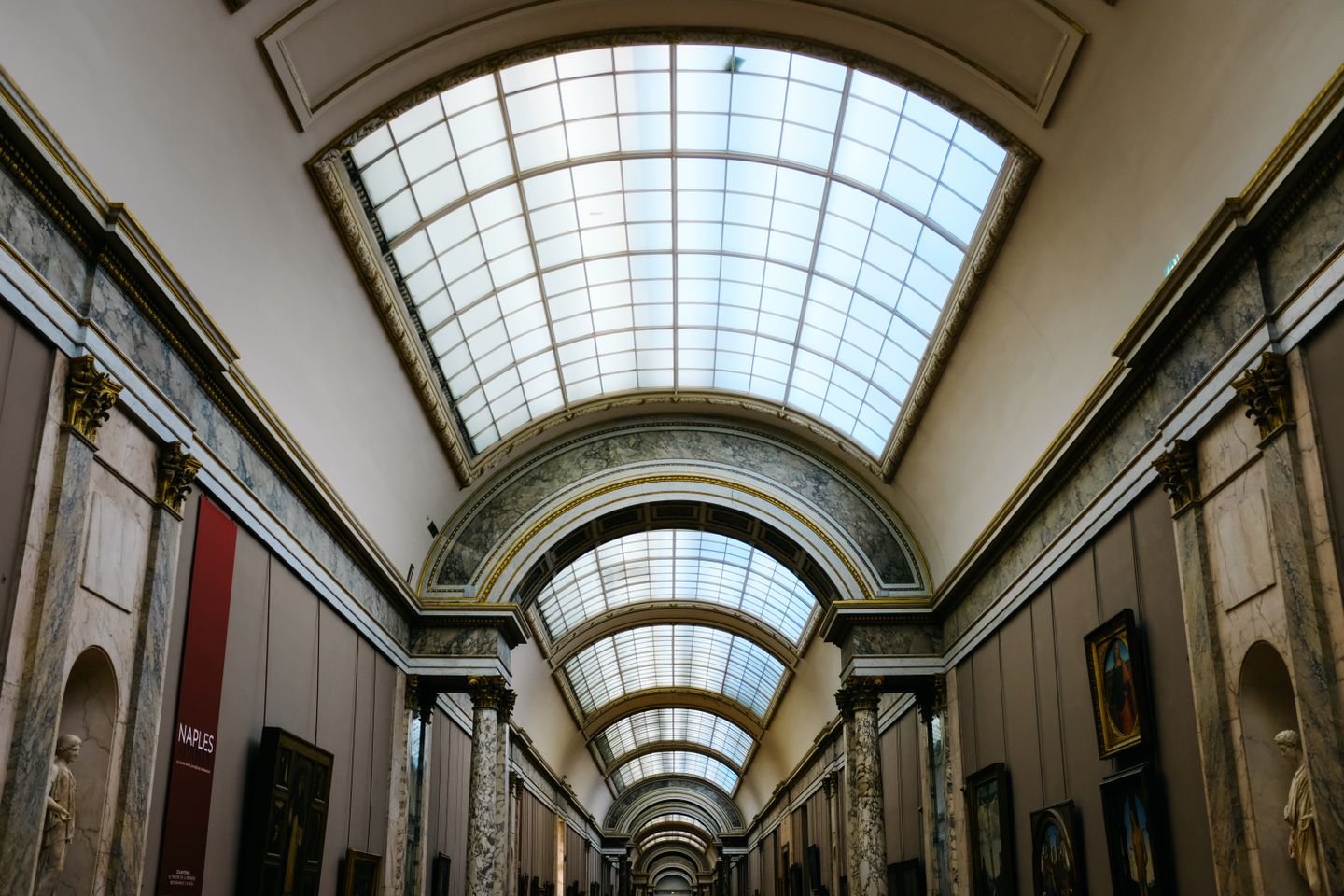 Vista interior del gran pasillo del Museo del Louvre con un elegante techo de cristal.
