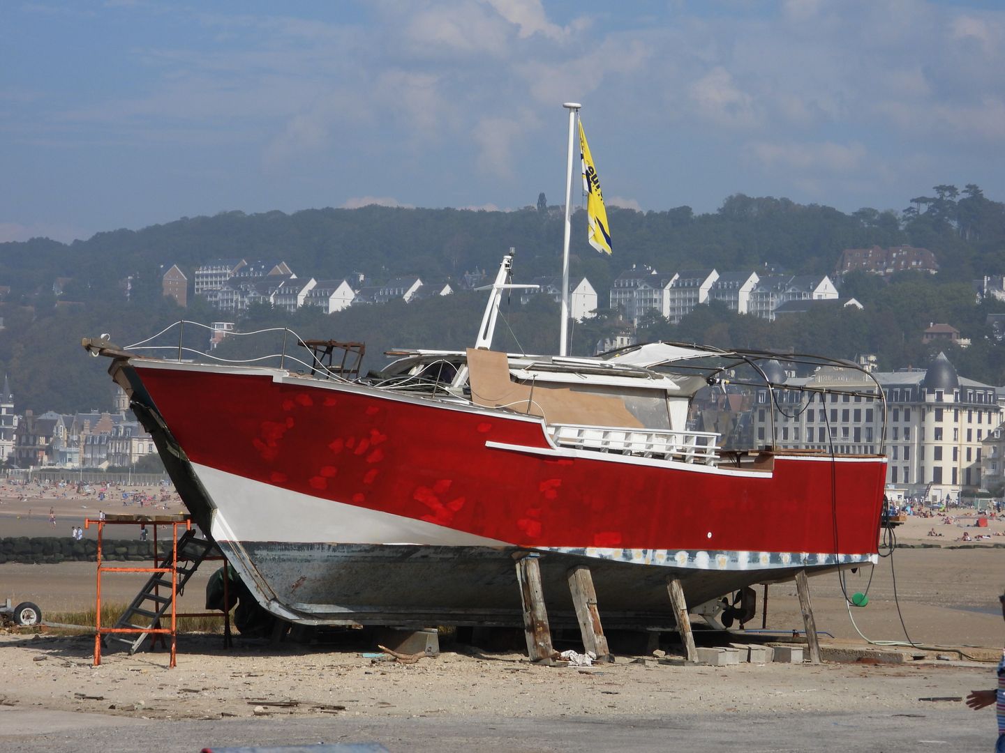 Un vibrante barco rojo atracado en la playa de Deauville, Normandía, con casas en el fondo bajo un cielo despejado.
