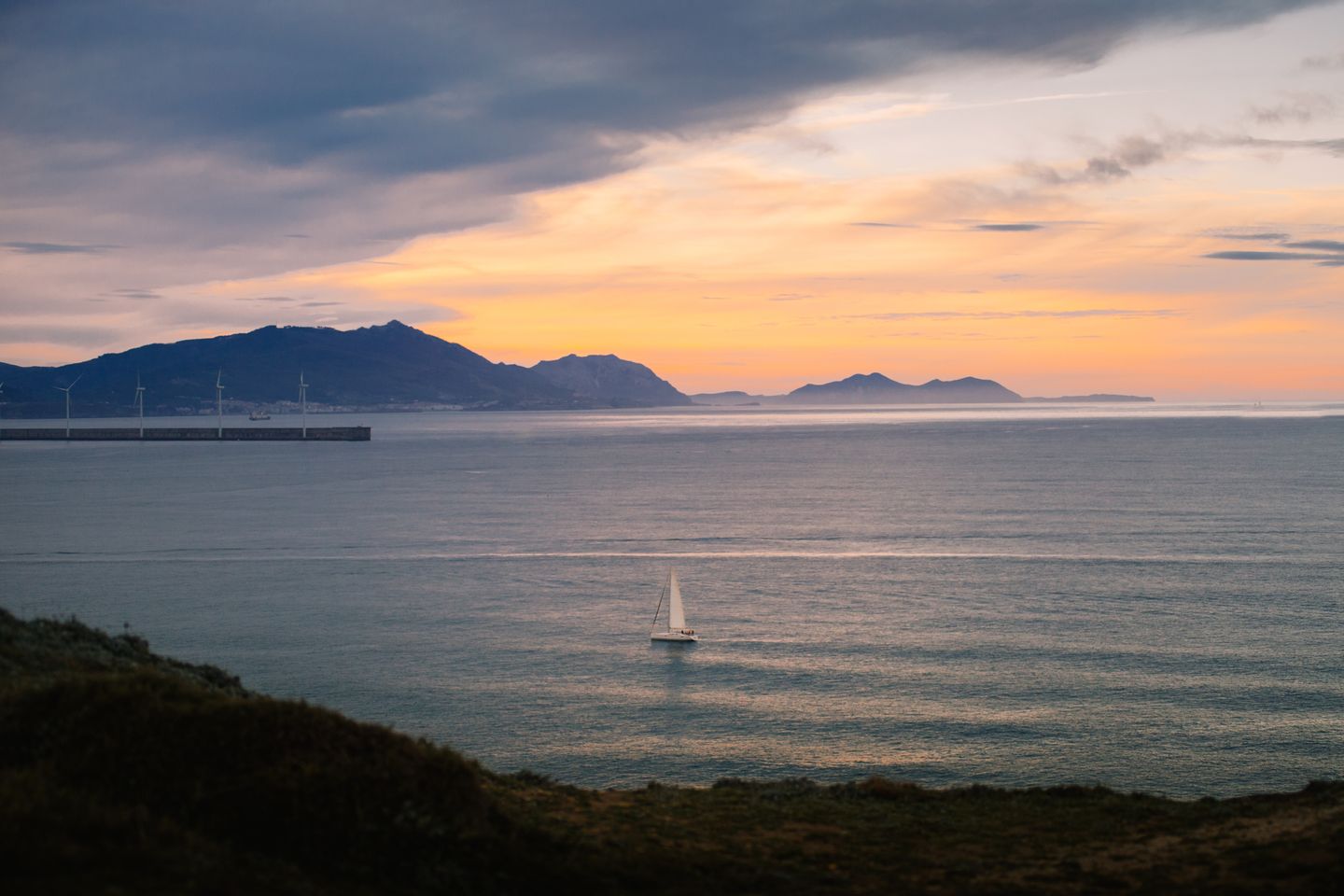 Vista escénica de un velero al atardecer cerca de la costa de Bilbao con montañas de fondo.