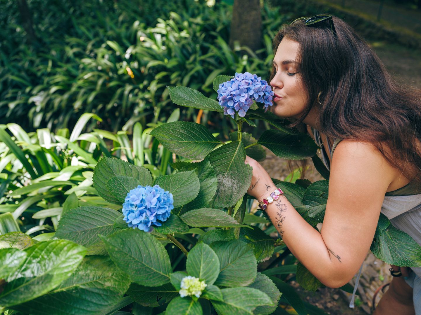 Una mujer olfateando vibrantes hortensias azules en un jardín exuberante en Funchal, Madeira, Portugal.