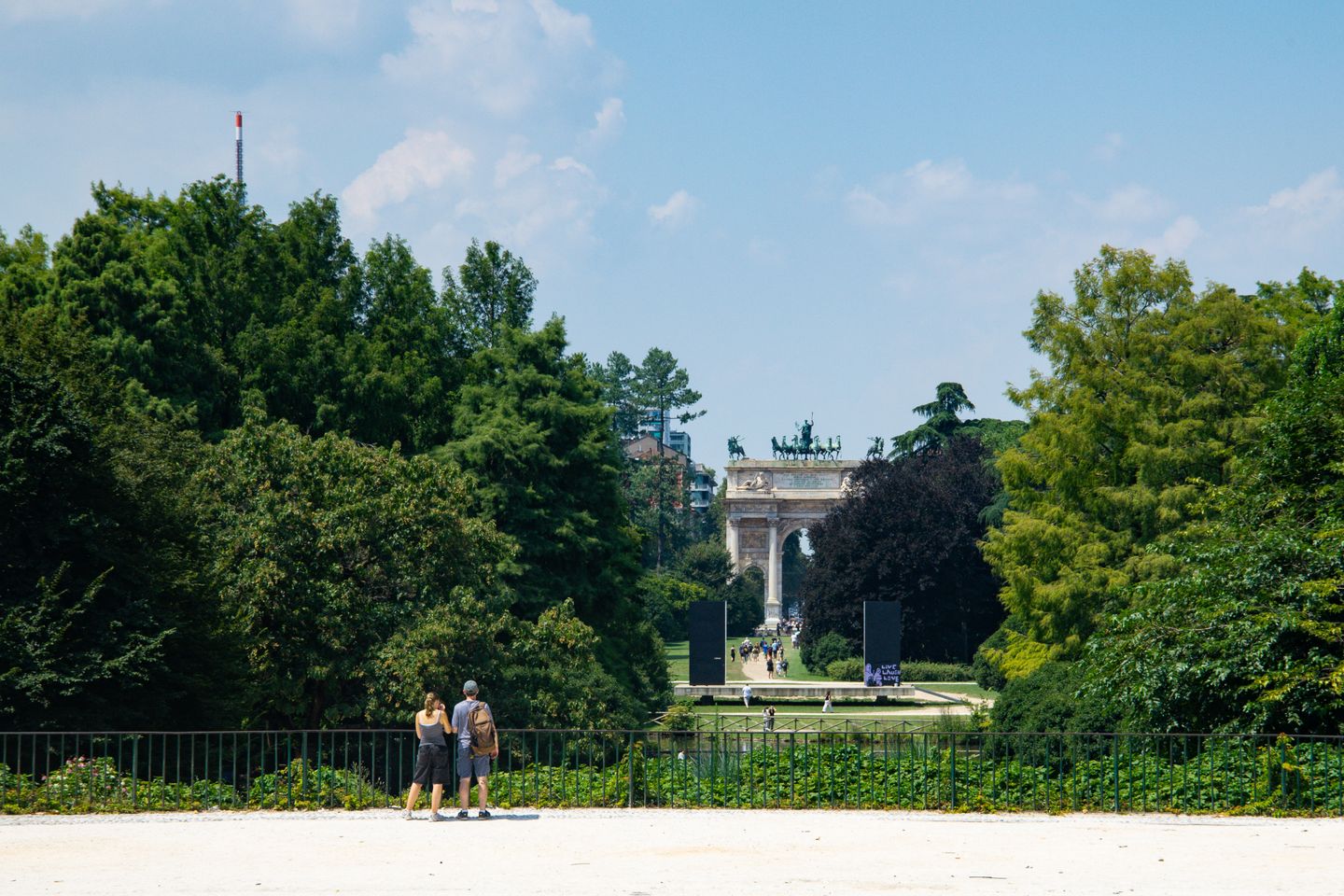 Personas disfrutando de un día soleado en el Parque Sempione con el icónico Arco de la Paz en Milán.