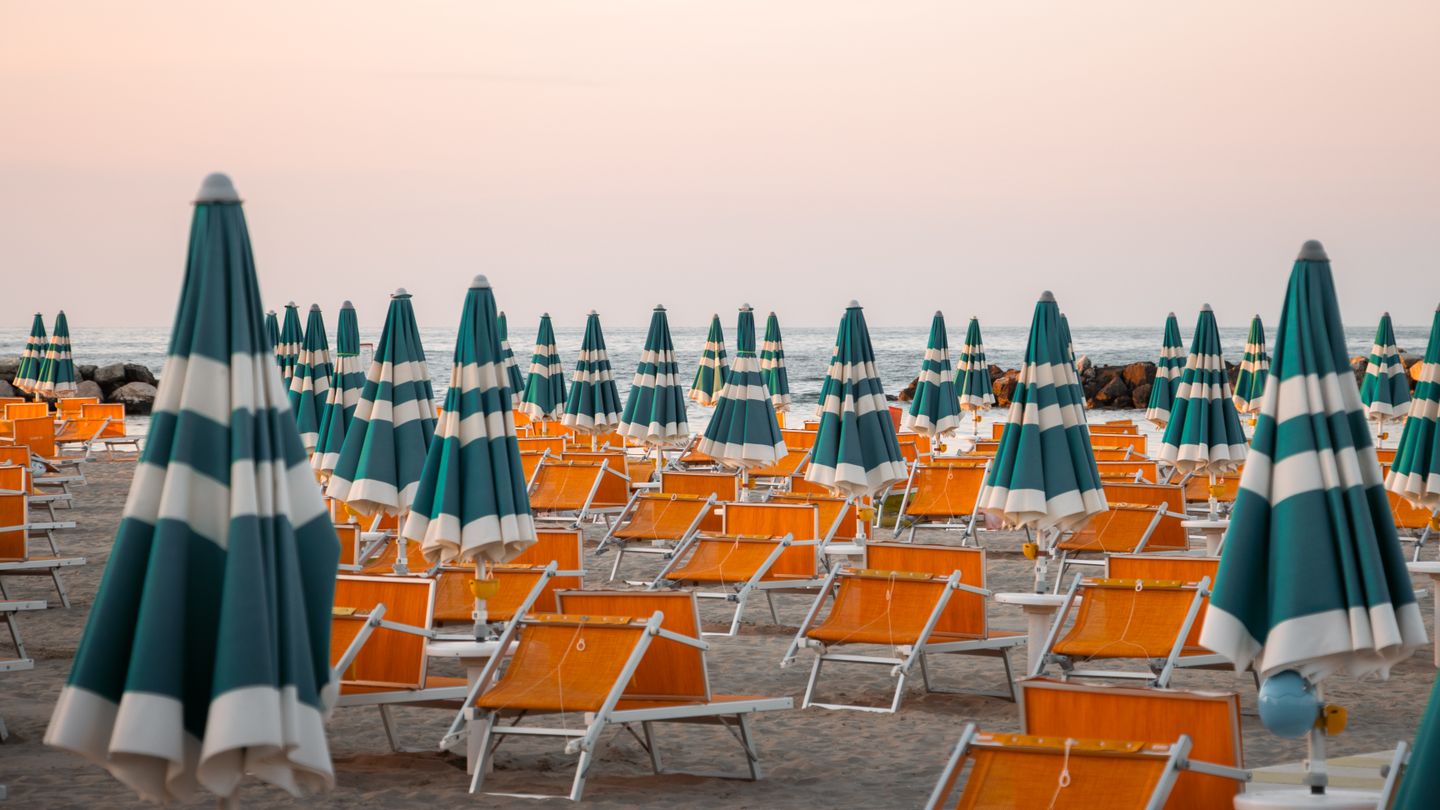 Sombrillas de rayas coloridas y sillas en la playa de Rimini durante el atardecer, perfectas para el ambiente veraniego.