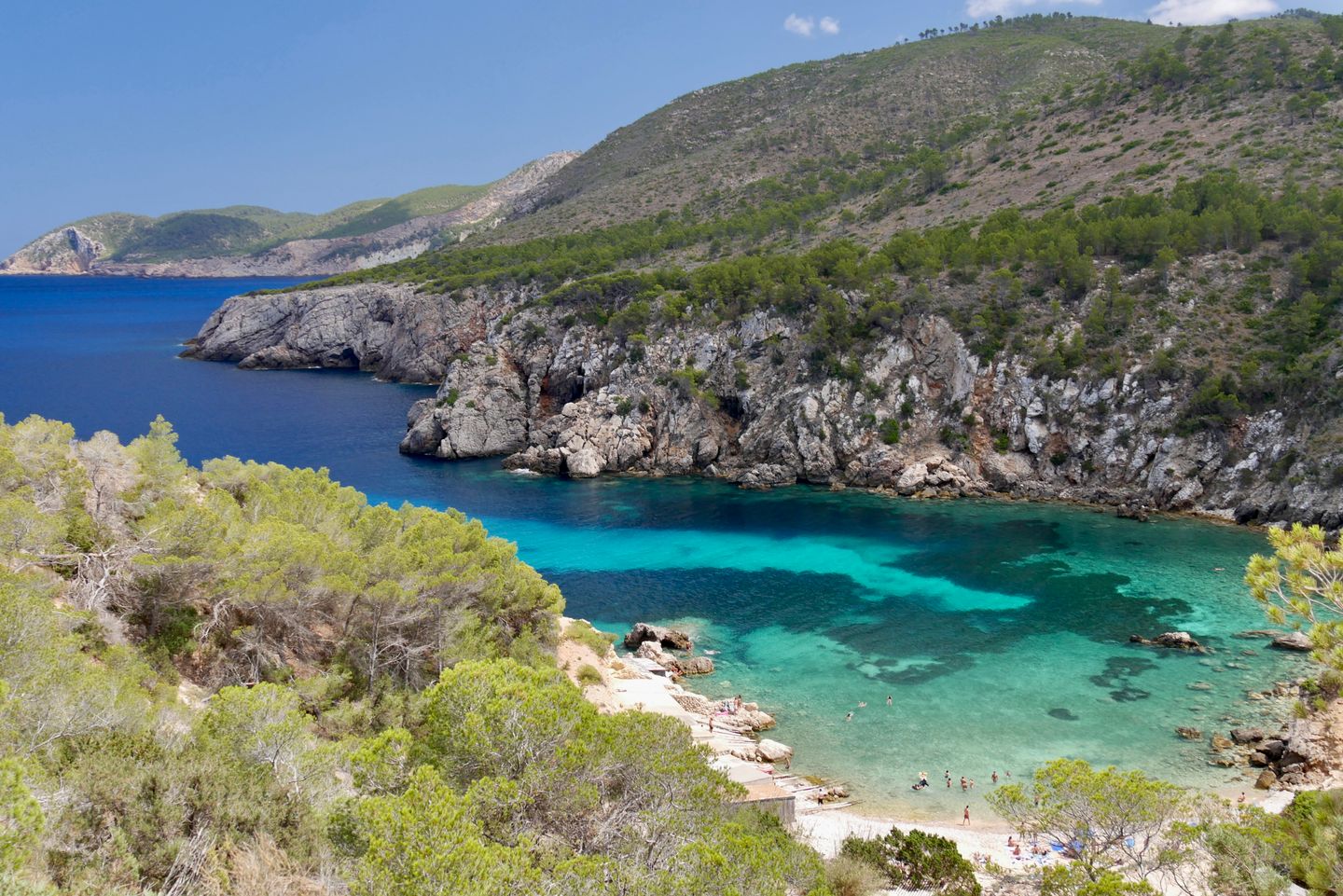 Aguas turquesas prístinas y costa rocosa de una playa aislada en Ibiza, perfecta para aventuras de verano.