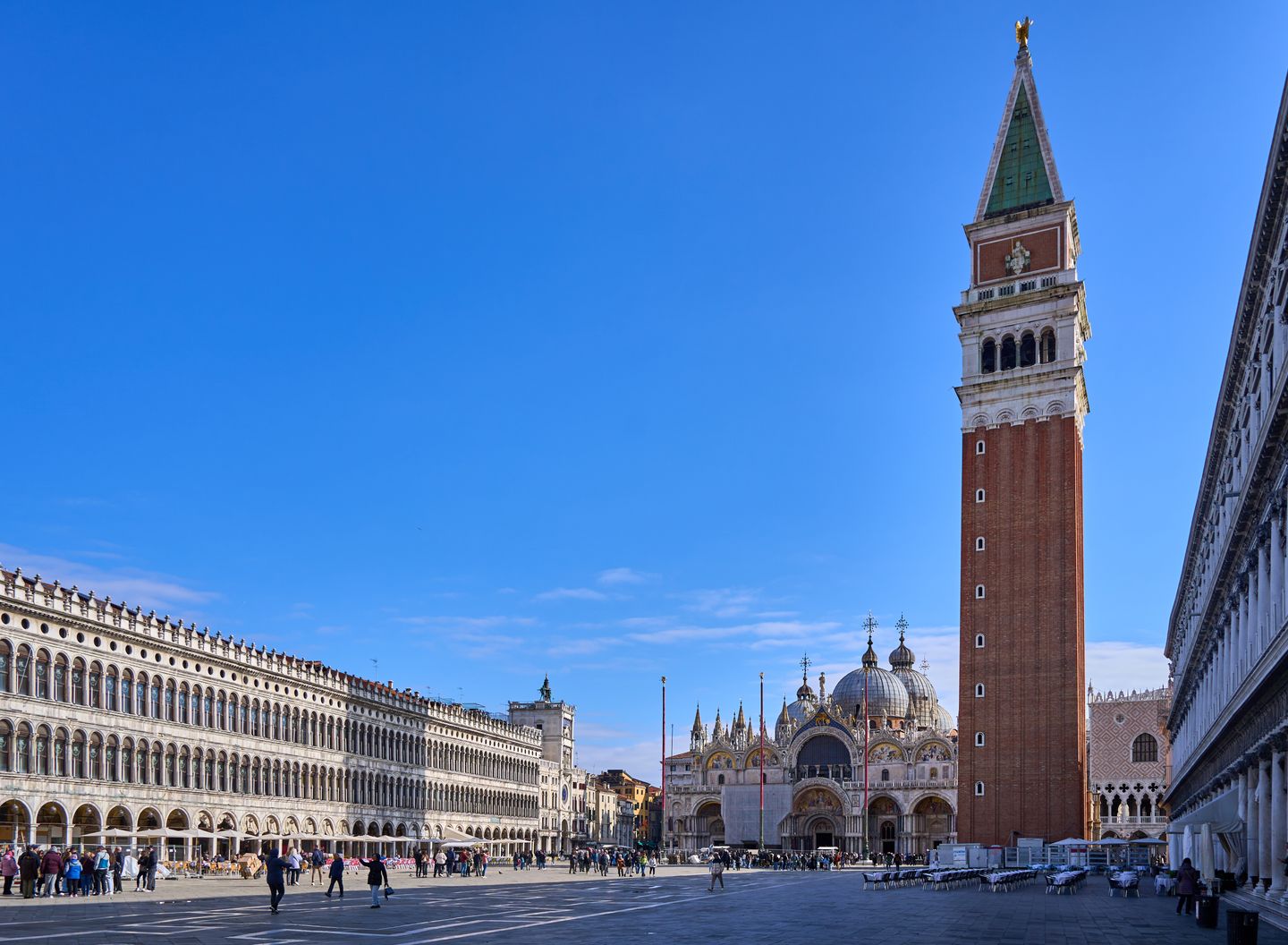 El Campanile y la Basílica de San Marcos en la icónica Plaza de San Marcos de Venecia bajo un cielo azul claro.