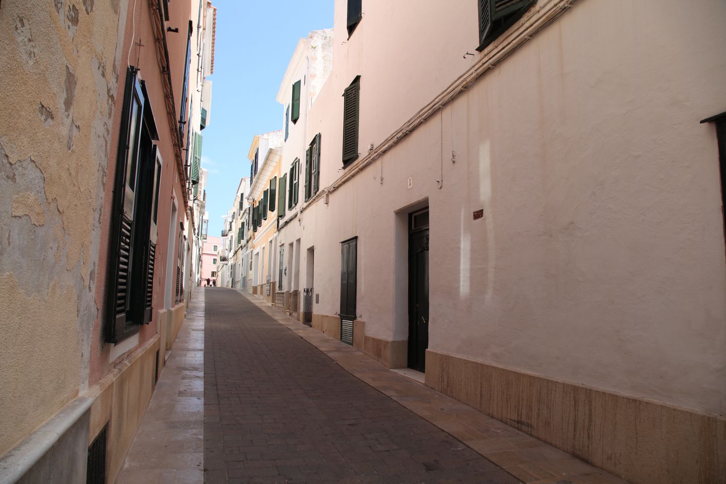 Pintoresca calle estrecha con edificios tradicionales en Ciudadela de Menorca, bajo un cielo azul claro.