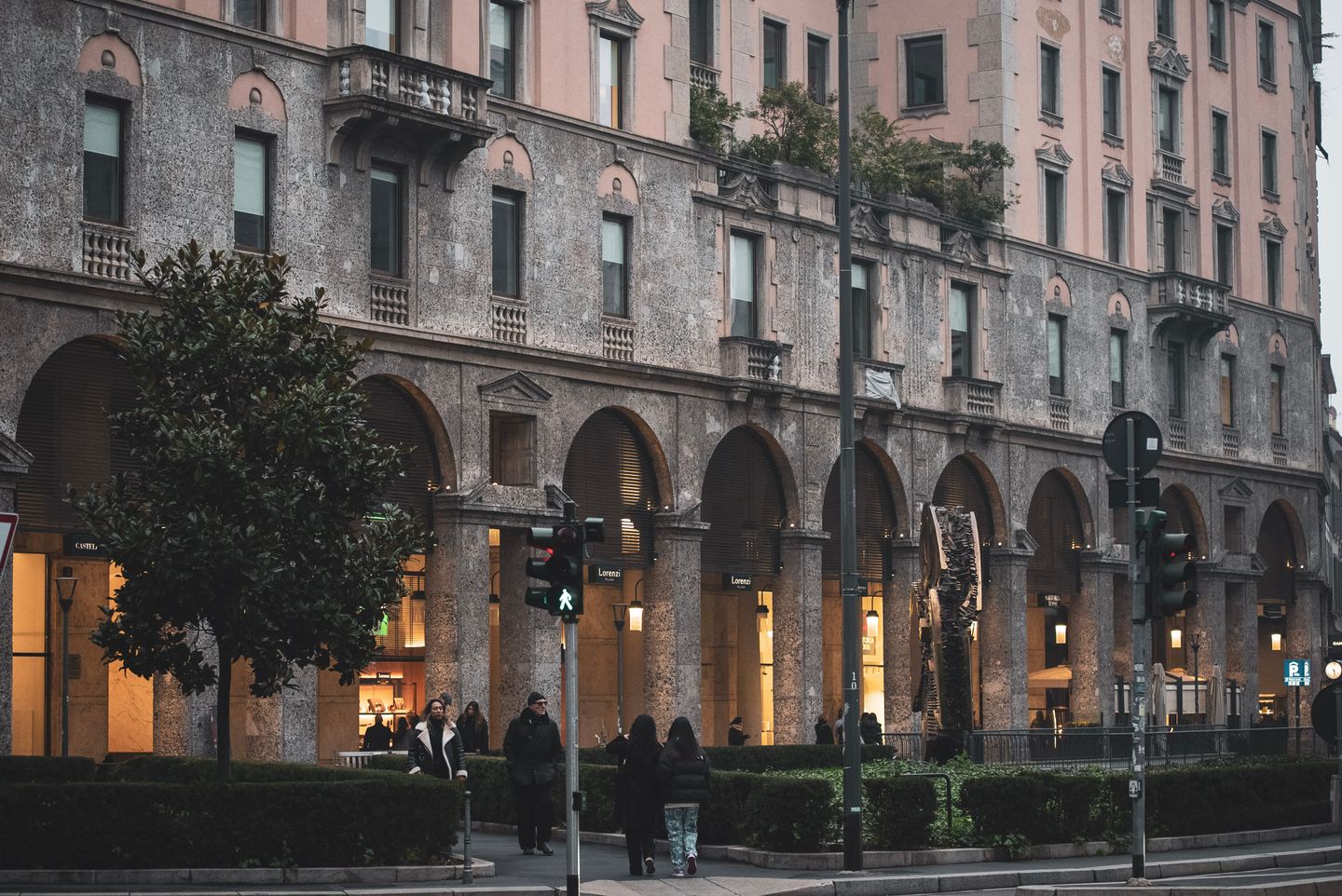 Encantadora arquitectura histórica en una calle de la ciudad en Milán, Italia, con peatones y vegetación exuberante.