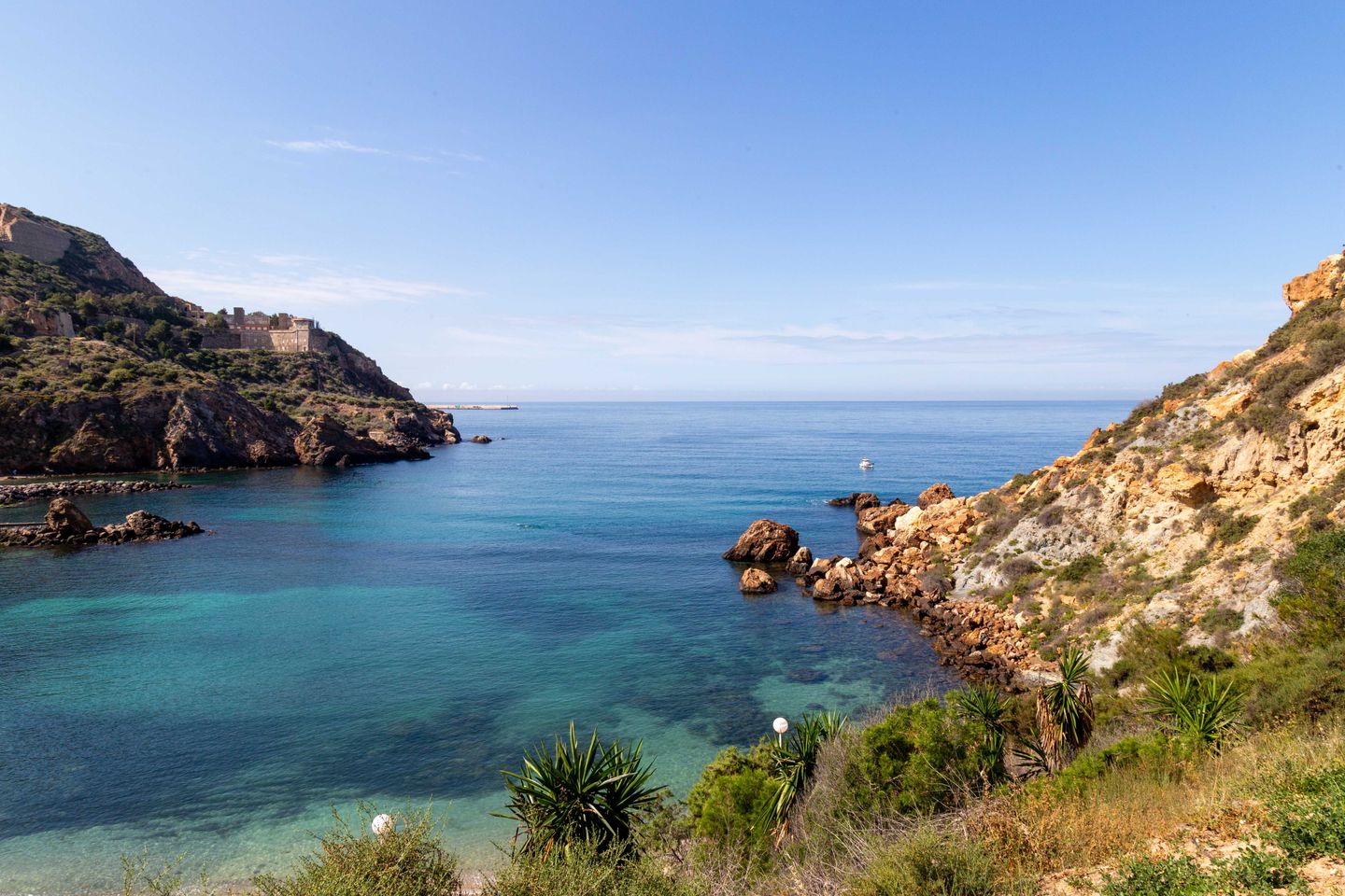 Vista escénica de un paisaje costero rocoso en Murcia, España, con aguas azules claras y vegetación.