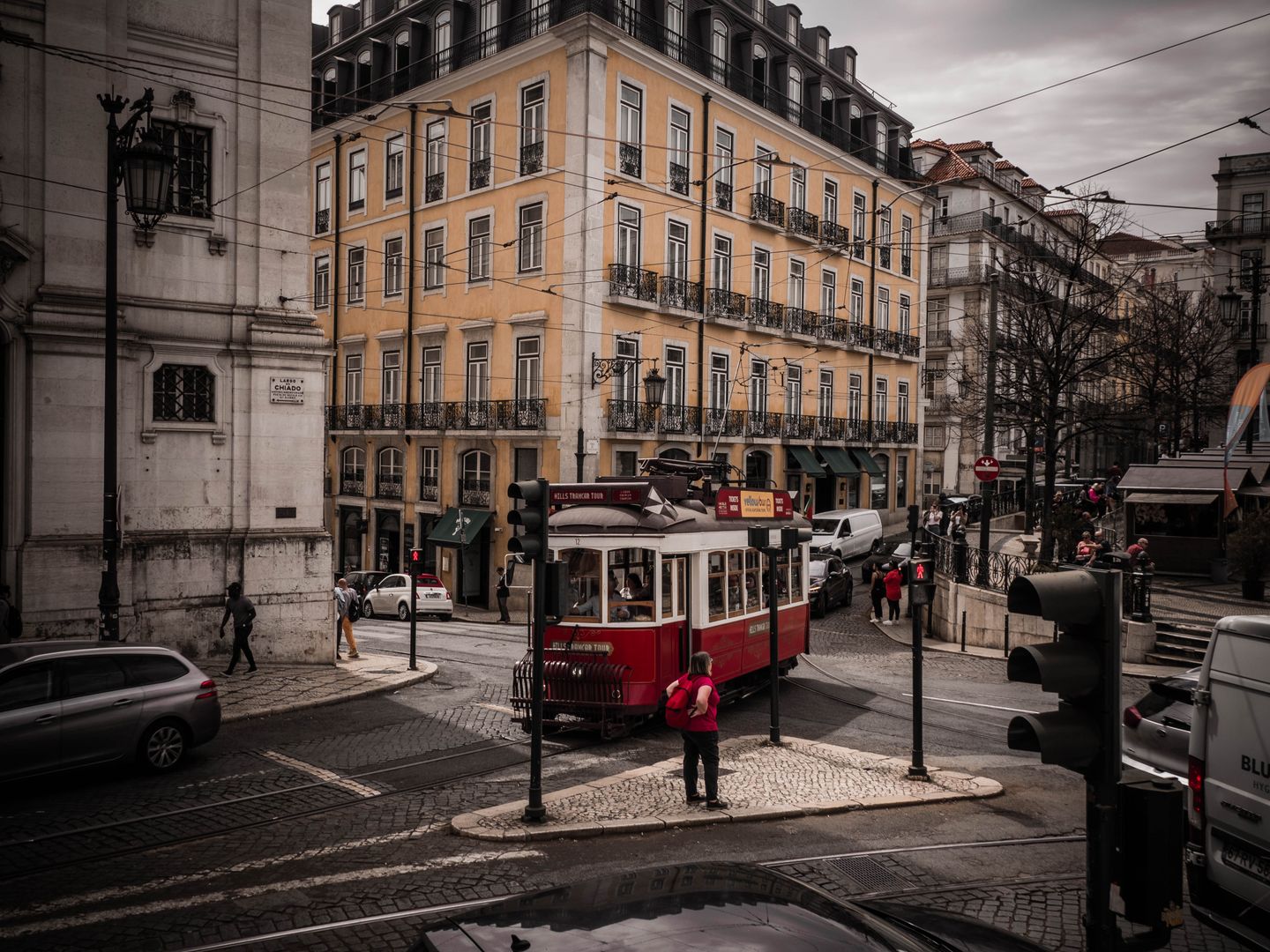Un tranvía rojo histórico circula por una encantadora calle del bullicioso centro de Lisboa, mostrando una arquitectura clásica.