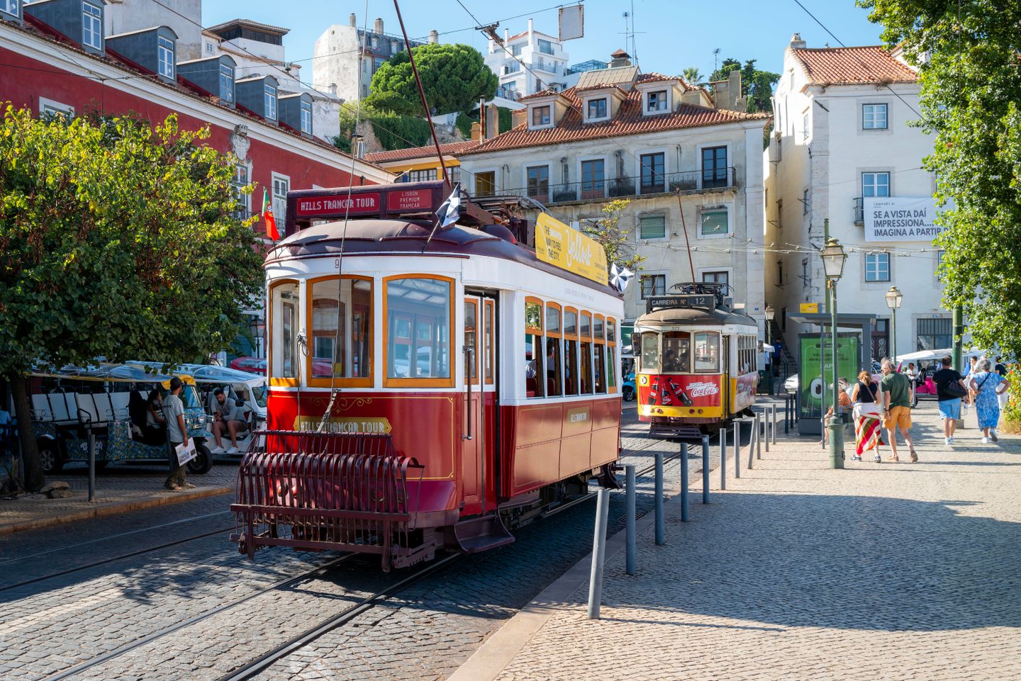 Tranvías vintage en el histórico barrio de Alfama de Lisboa, mostrando arquitectura icónica y turismo de verano en Portugal.