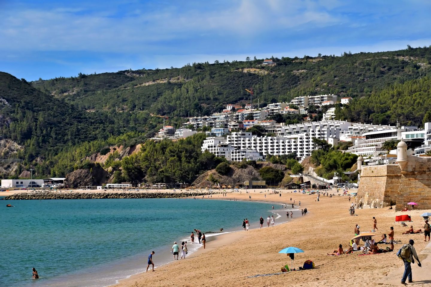 Hermosa escena de playa en Sesimbra, Portugal, con una costa vibrante y edificios en la colina.