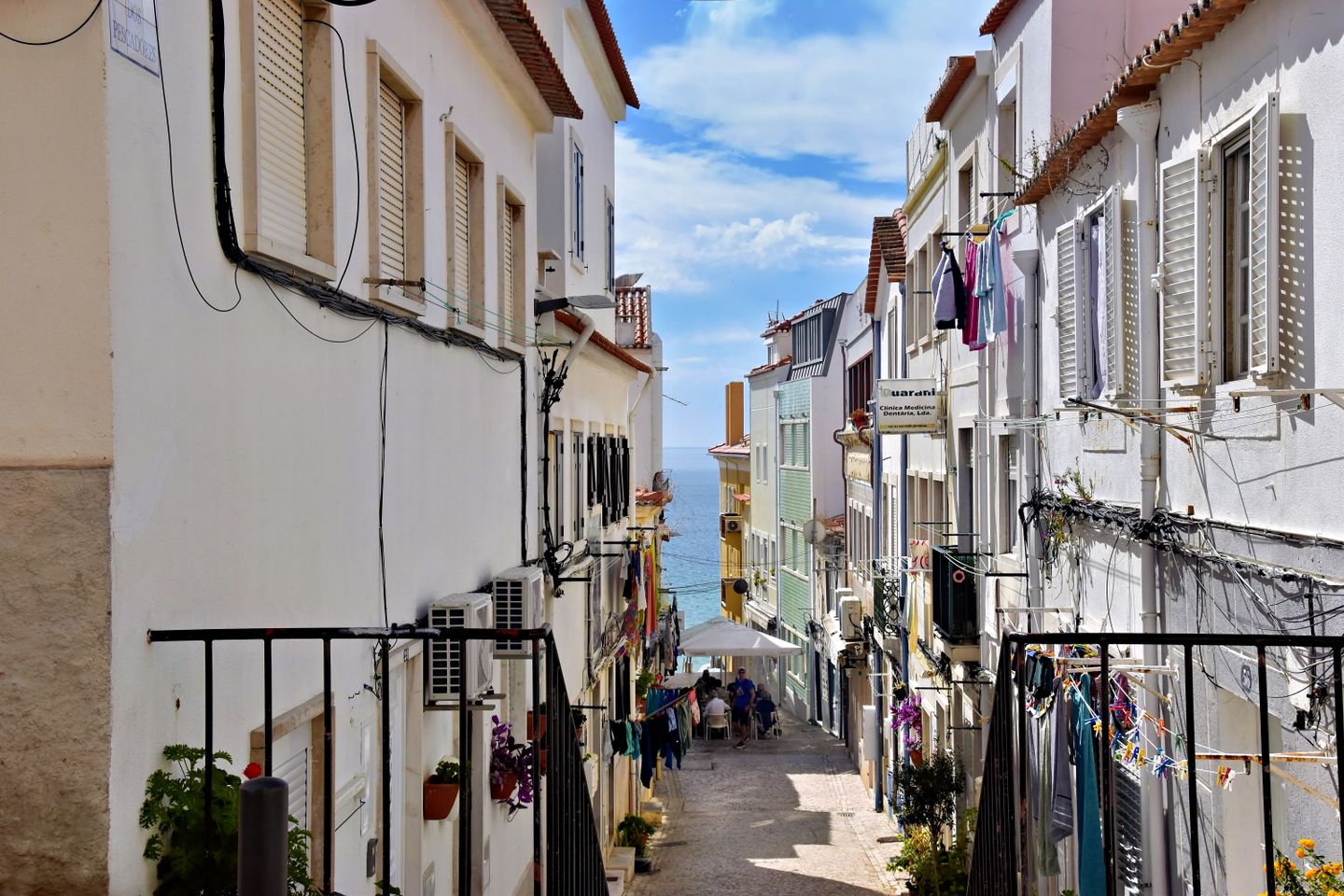 Calle pintoresca en Sesimbra, Portugal, mostrando edificios coloridos y vista al océano.