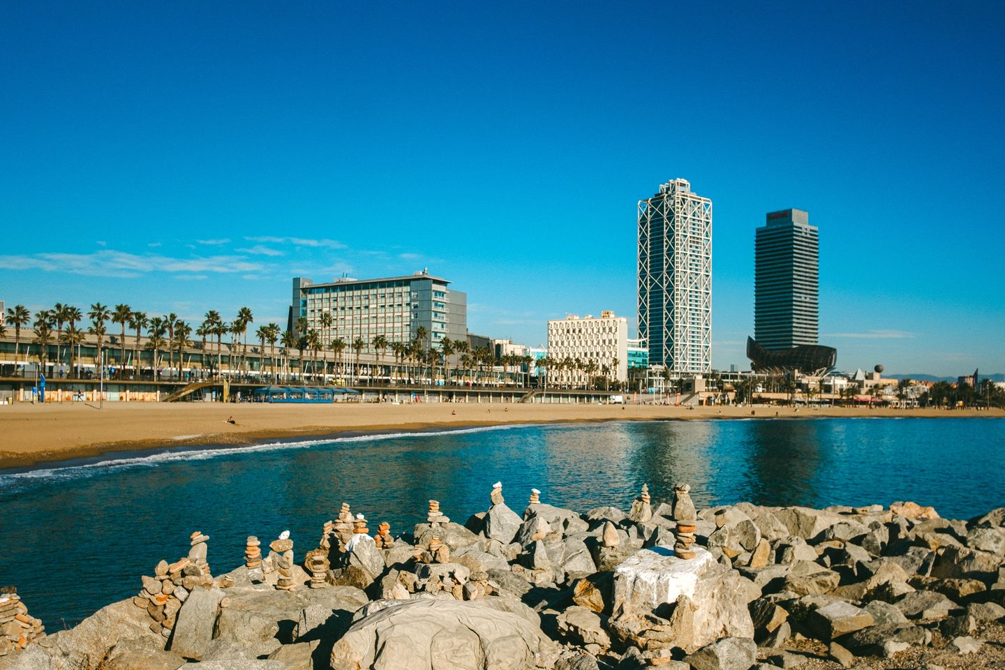 Vista soleada del icónico litoral de Barcelona con rascacielos y formaciones rocosas.