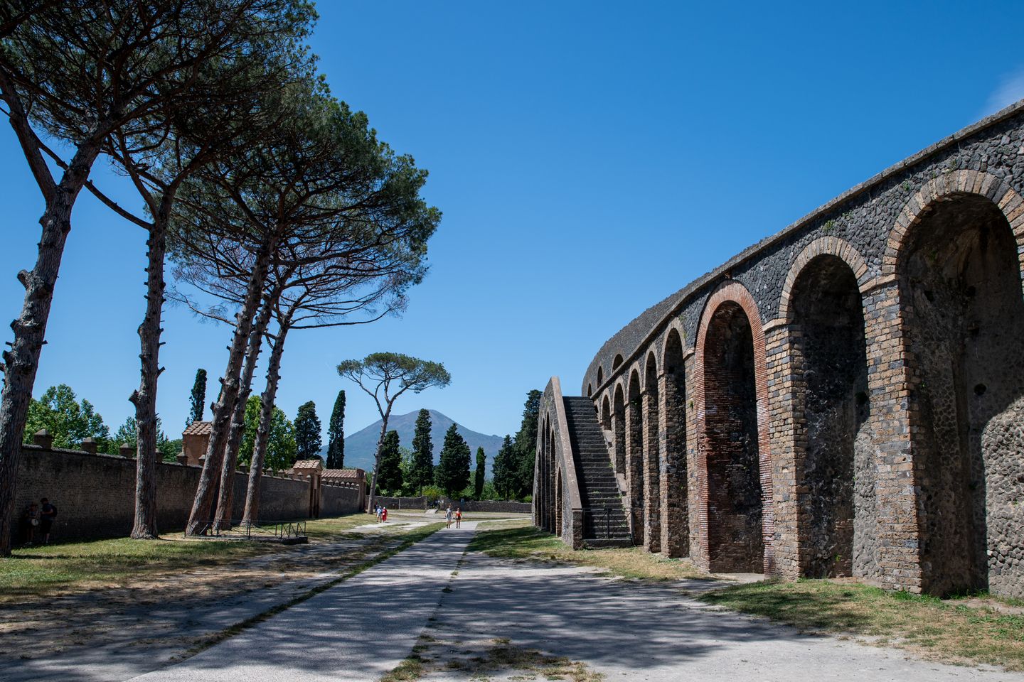 Explora las antiguas ruinas de Pompeya bajo cielos azules claros con el Monte Vesubio visible a lo lejos.