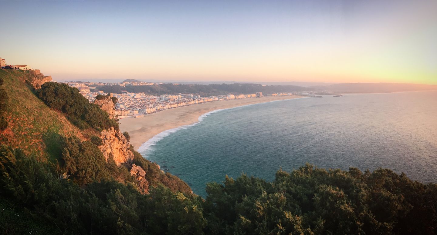 Impresionante vista de la playa de Nazaré y la costa al atardecer, capturando el pueblo y el océano bajo un cálido resplandor.