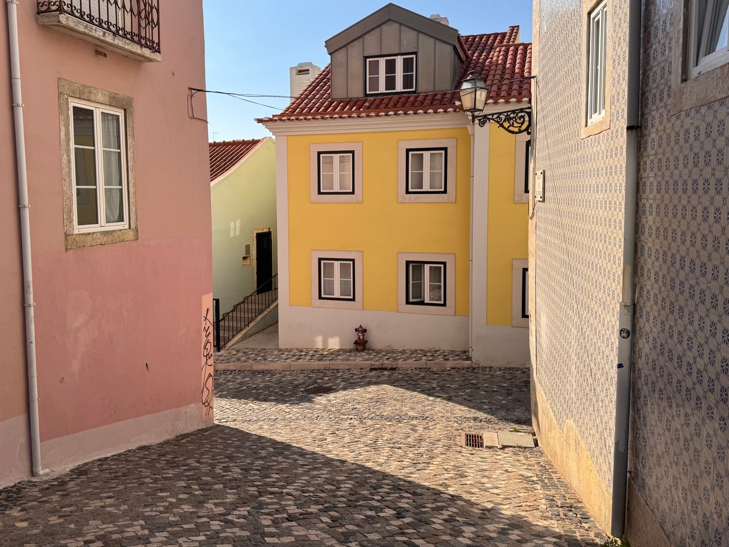Edificios vibrantes a lo largo de una rústica calle empedrada en el histórico barrio Alfama de Lisboa durante el día.