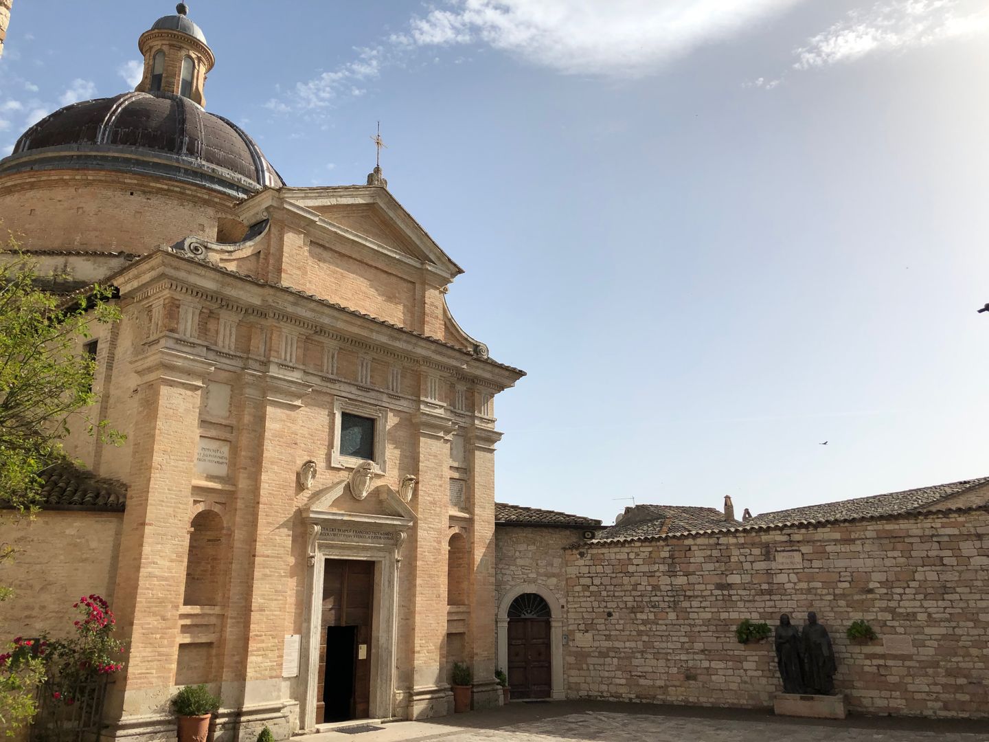 Vista exterior de una iglesia histórica en Asís, Italia, mostrando una arquitectura clásica bajo un cielo brillante.