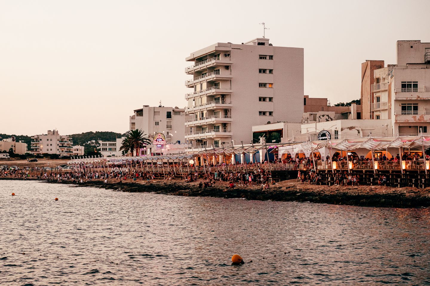 Escena animada del paseo marítimo de Ibiza que muestra la vibrante vida nocturna costera al atardecer.