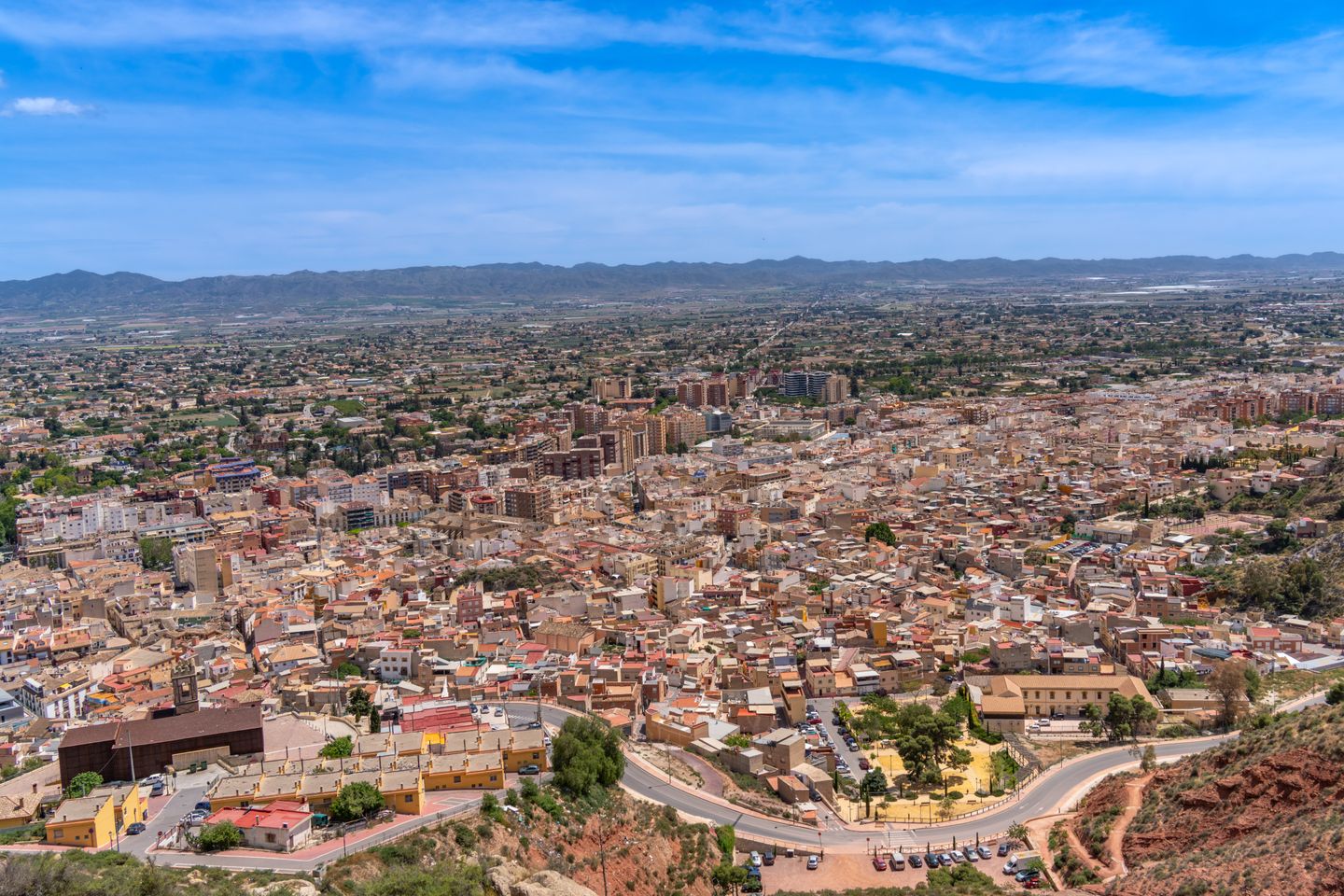 Vista aérea de Lorca, Murcia, España, mostrando la arquitectura y el paisaje de la ciudad bajo un cielo azul claro.