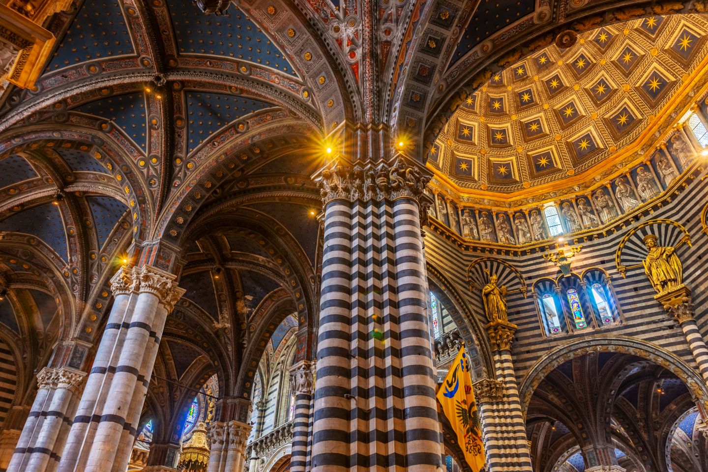 Impresionante interior de la Catedral de Siena, que muestra una detallada arquitectura gótica bajo una cúpula estrellada.
