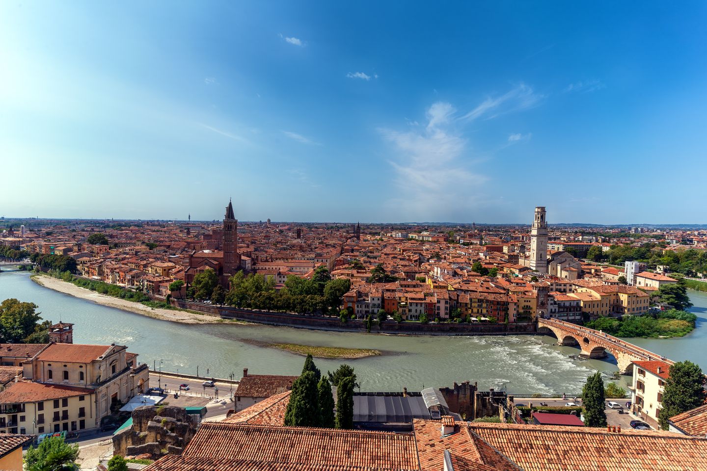 Impresionante vista aérea del paisaje urbano de Verona, con el río Adige serpenteando entre edificios históricos bajo un cielo azul despejado.