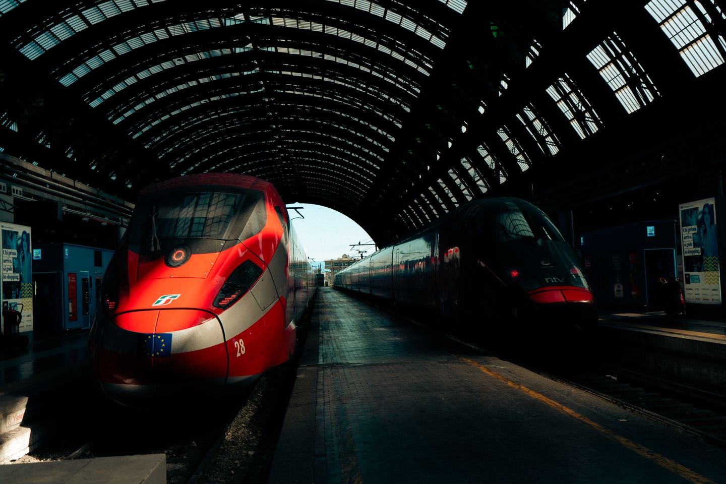 Vista dinámica de trenes de alta velocidad en la emblemática estación central de Milán bajo un techo de cristal.