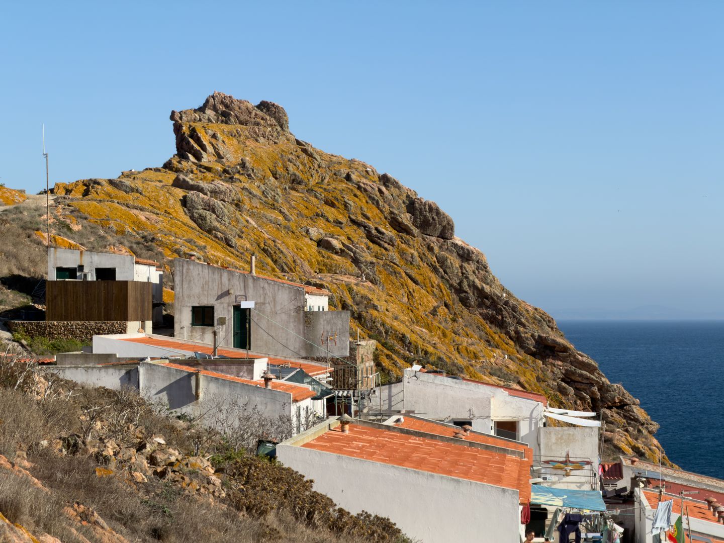 Vista panorámica de casas costeras contra un escarpado acantilado en Peniche, Portugal, bajo un cielo despejado de verano.