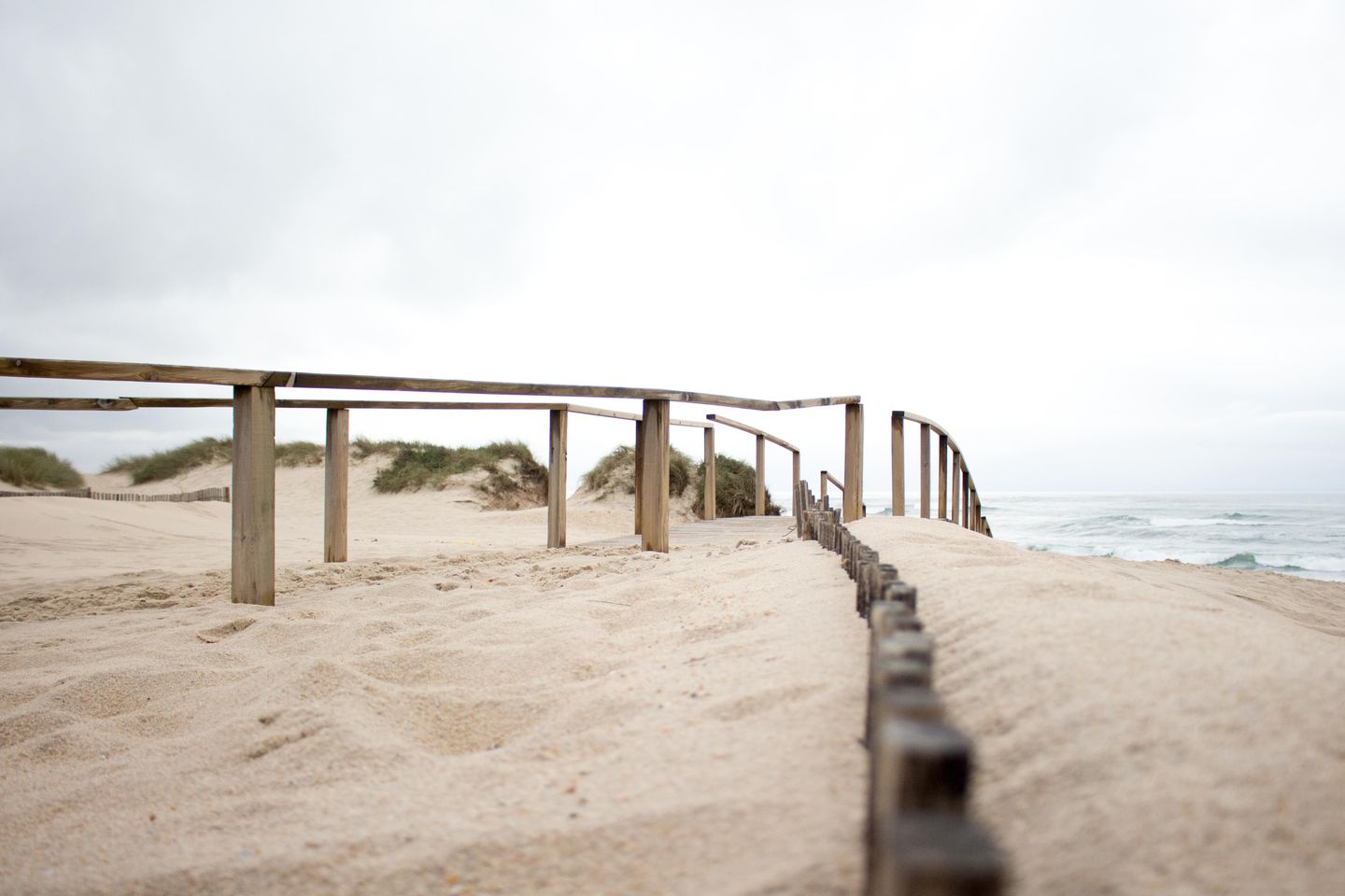 Vista escénica de un camino de arena con barandas de madera y olas del océano en Aveiro, Portugal.