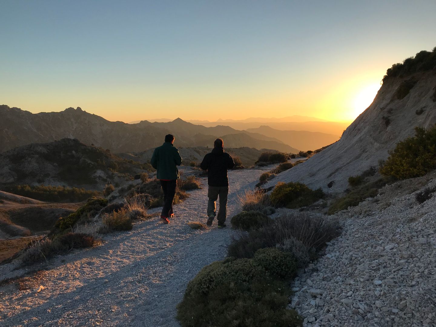 Dos excursionistas caminando por un sendero en Sierra Nevada, España al amanecer con una impresionante vista de la montaña.