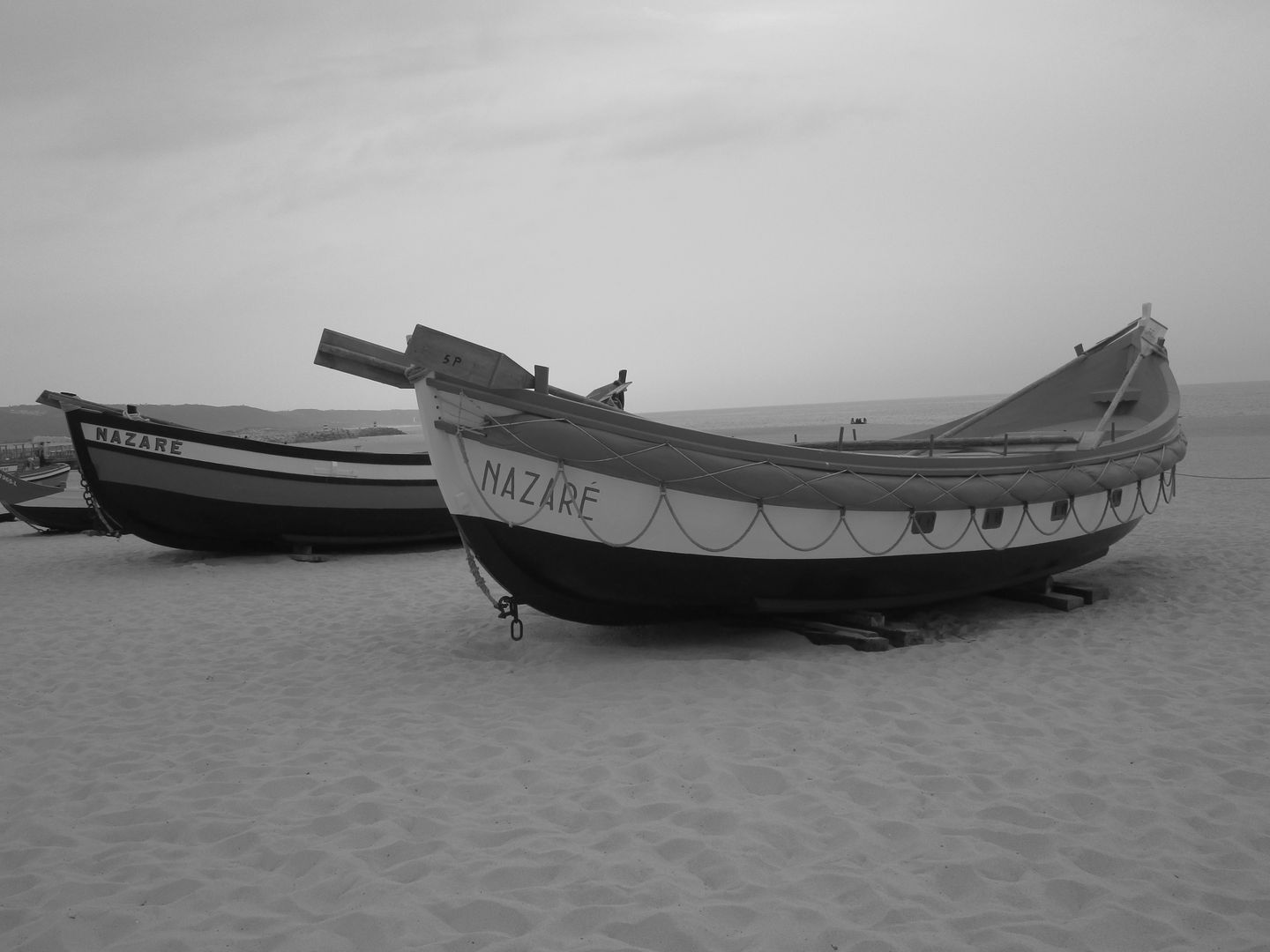 Foto en blanco y negro de barcos de pesca tradicionales en la playa de Nazaré, Portugal.