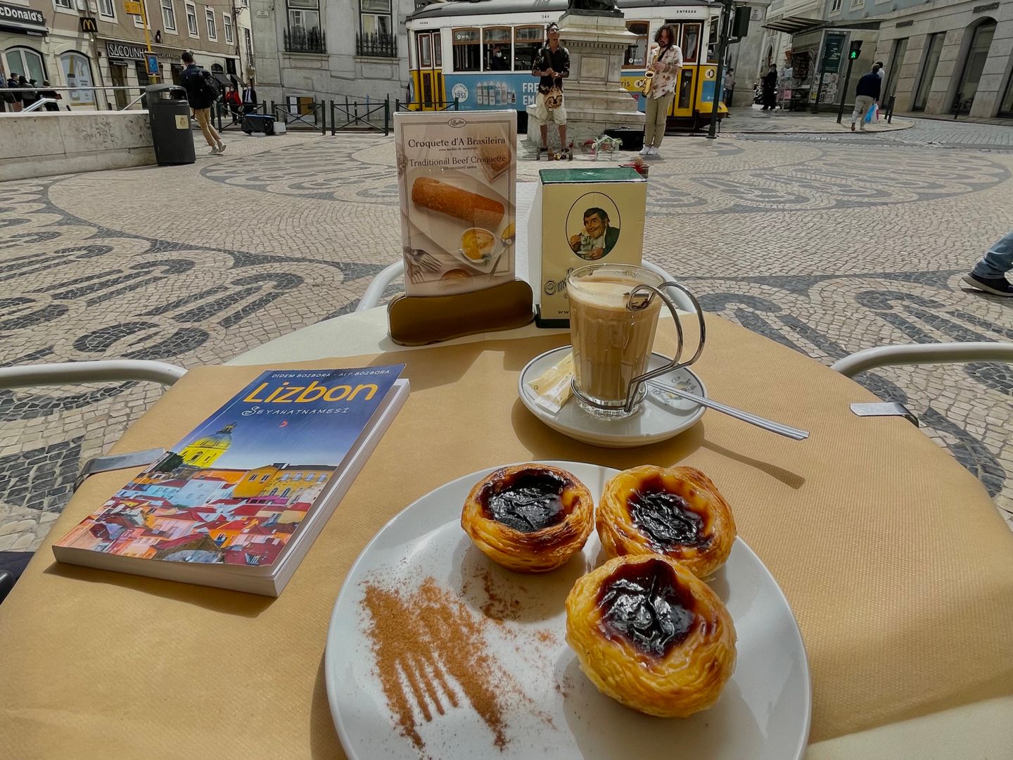 Degustando Pastéis de Nata con café en un café de Lisboa, con el icónico tranvía de fondo.